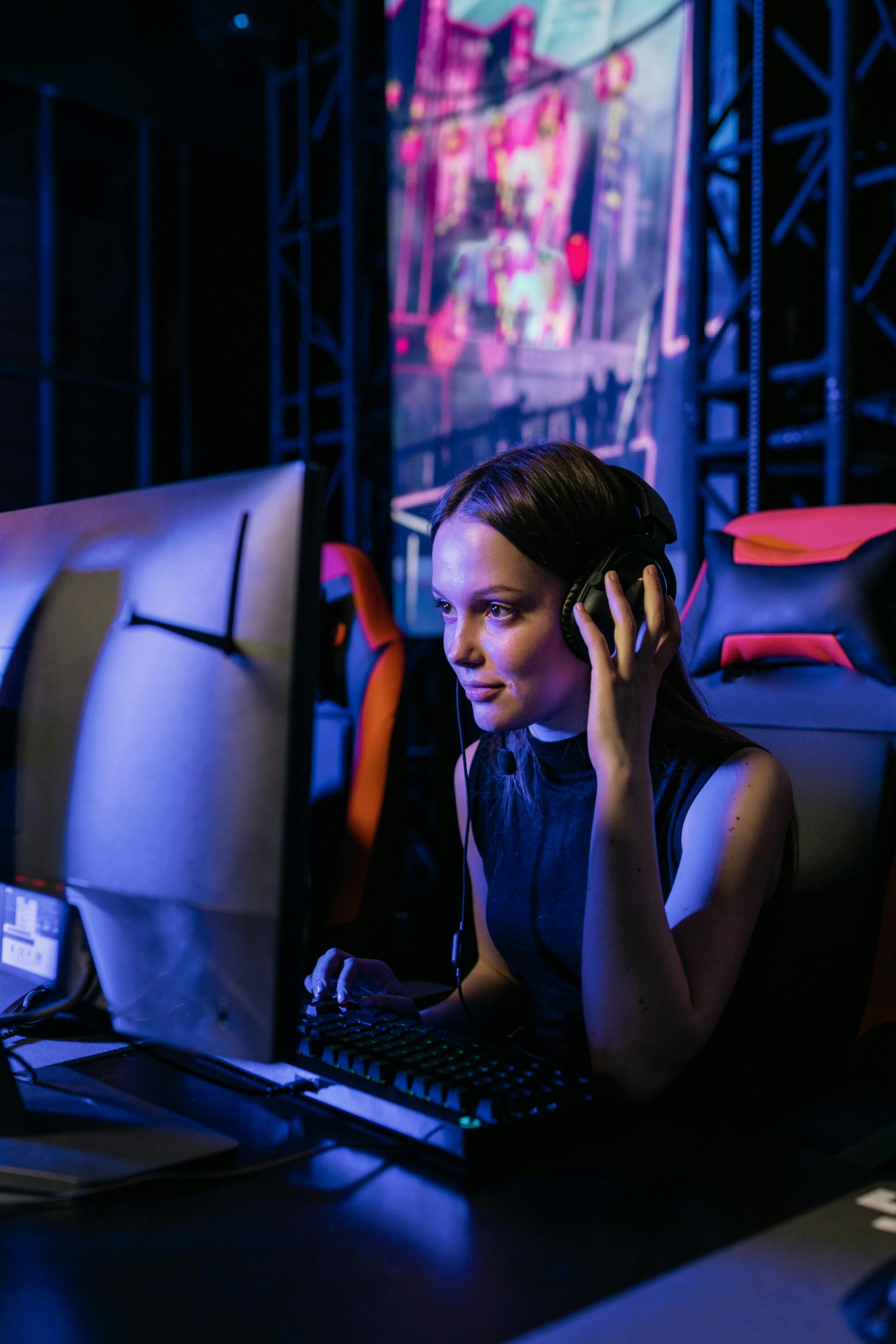 A woman gamer with a headset deeply focused on playing video games in an community driven esports arena. Gaming on a custom build PC from Steehl Systems.